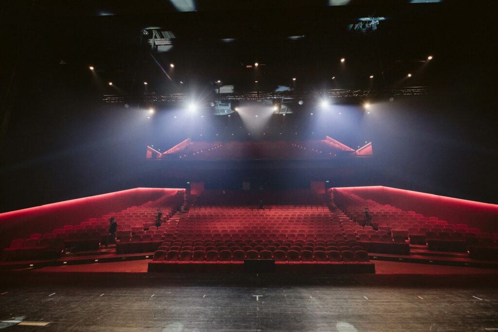 View of the audience from the stage. The seats in the audience are red and currently empty.